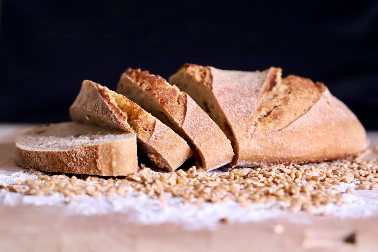 Close-up of sliced artisan bread on a rustic wooden board with flour and wheat grains.